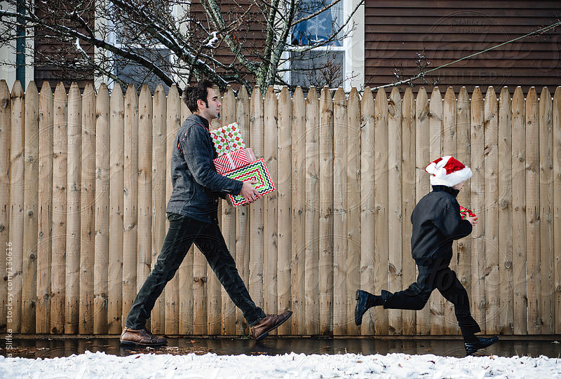 Boy runs ahead of his dad as they carry Christmas presents by Cara Slifka