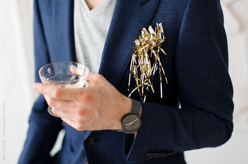 Young man in navy suit holding champagne glass at a party with tinsel on white background. by Tru Studio