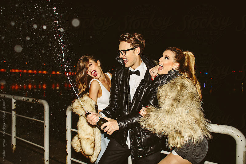 Three friends opening champagne in night out. by Studio Firma