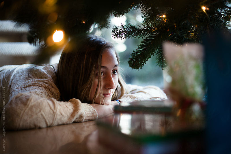 Teenage girl looking at the Christmas presents under the tree by Carolyn Lagattuta